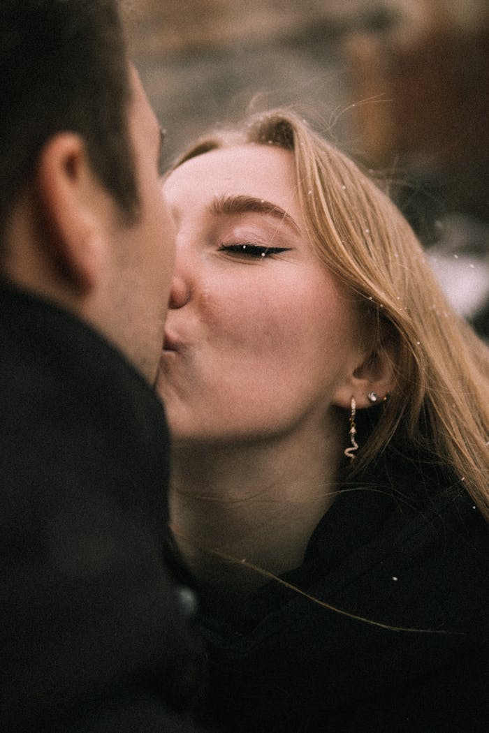 Close-up of a couple sharing a tender kiss, wrapped in winter attire, conveying warmth and affection.