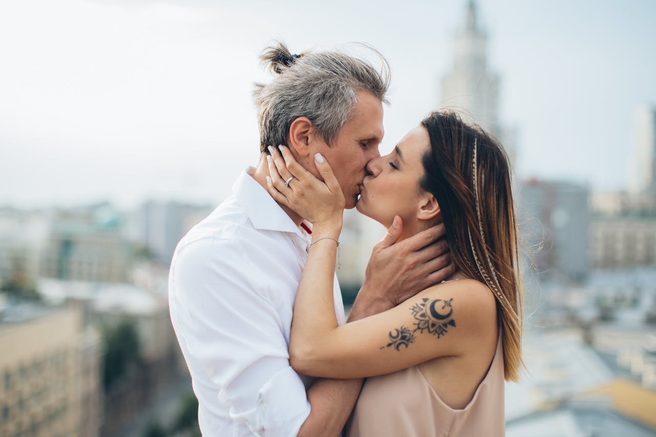 An intimate moment between a couple kissing outdoors with a cityscape backdrop.